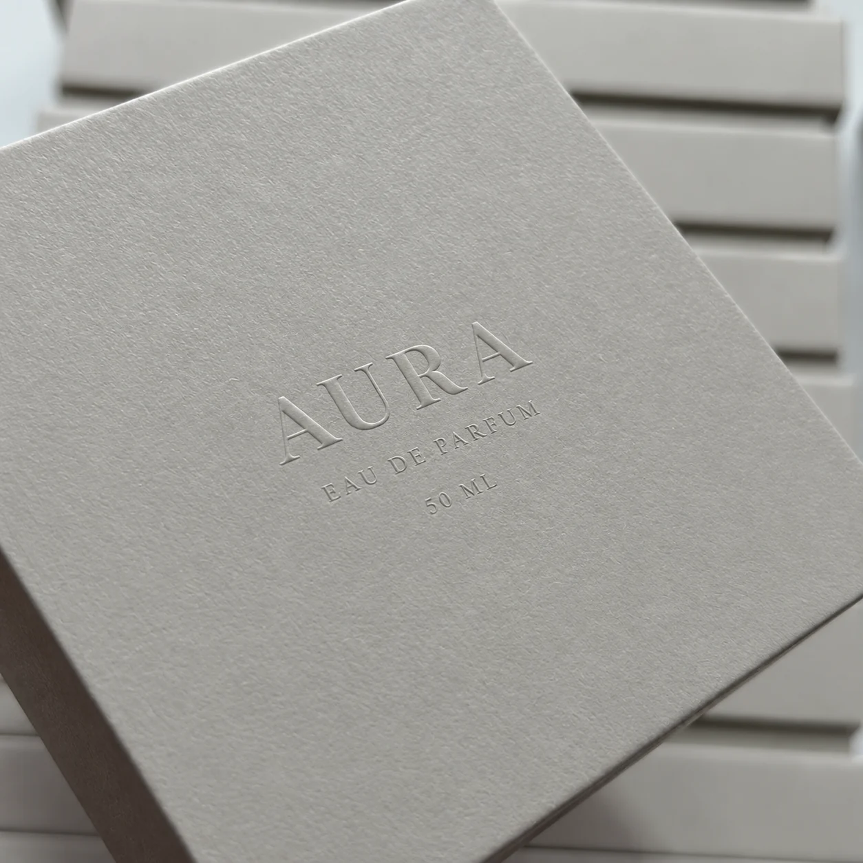 Light gray textured perfume box with debossed logo