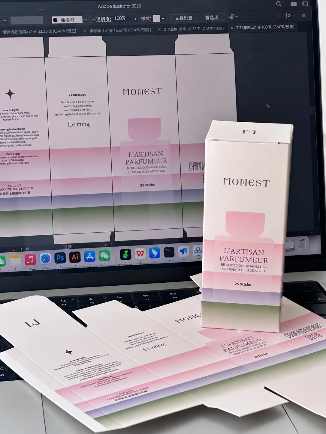 Printed incense carton and flat artwork sheets beside a monitor