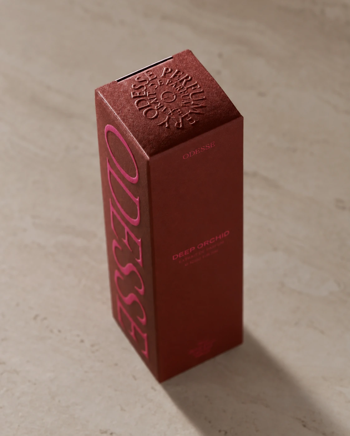 Brown perfume carton with raised lettering on the top panel