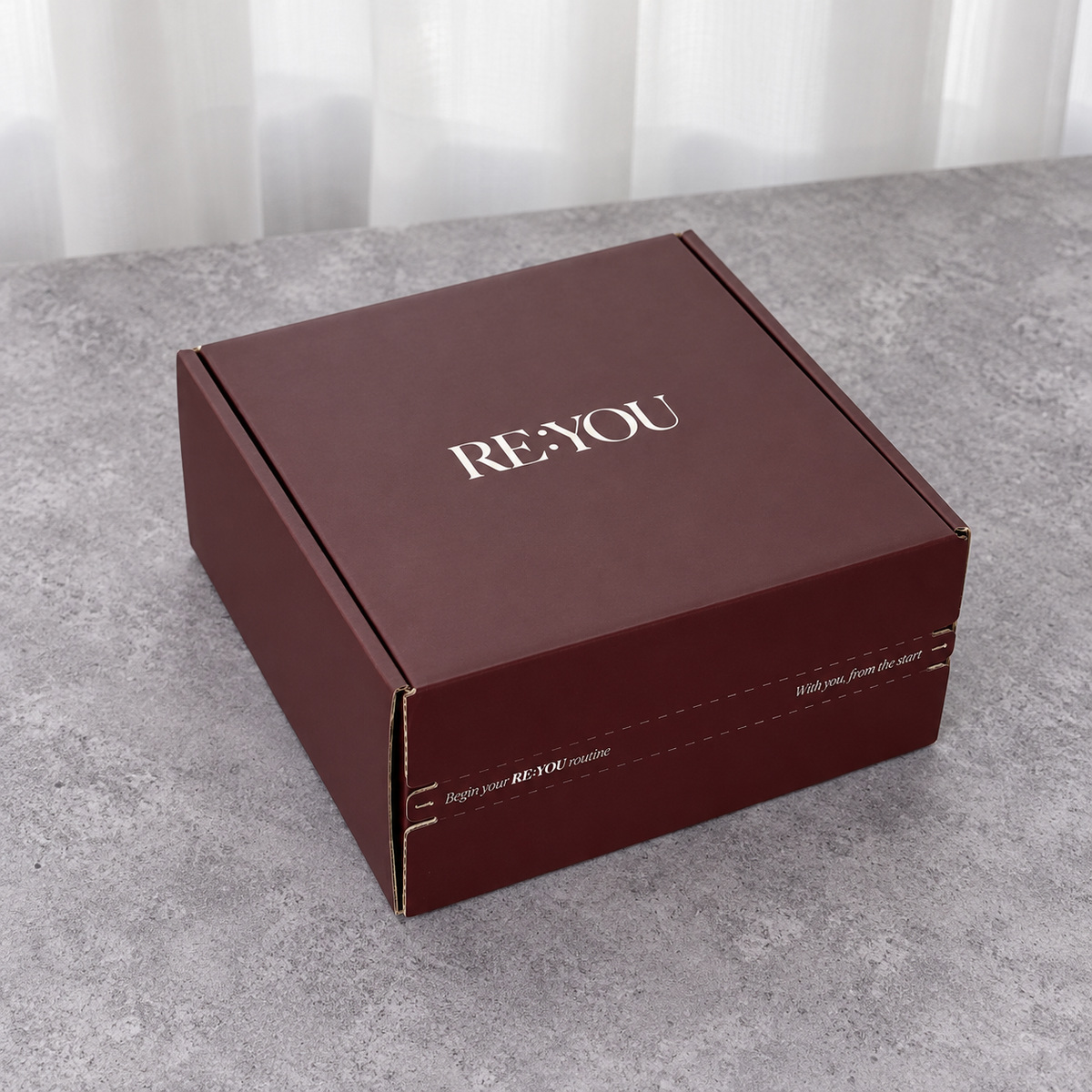 Closed burgundy folding mailer box with white logo and front tear-strip opening