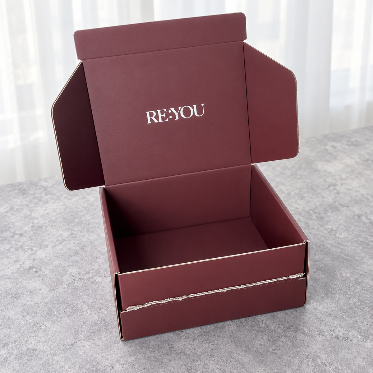 Open burgundy mailer showing the torn front strip, hinged lid and empty interior