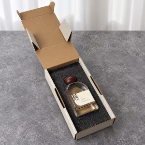 Open cream long perfume mailer box with a bottle fitted into a black foam insert