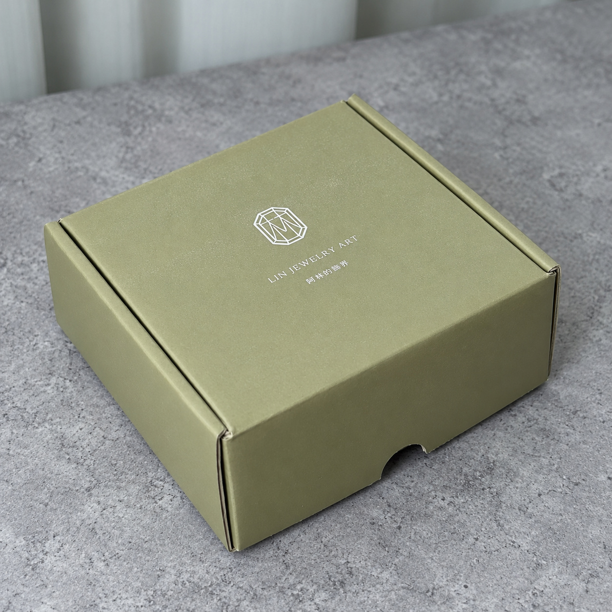 Olive green fold-flat mailer box with silver foil logo on a white background
