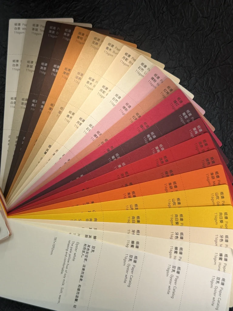 A fan of warm-colored paper cards with printed color names and weights
