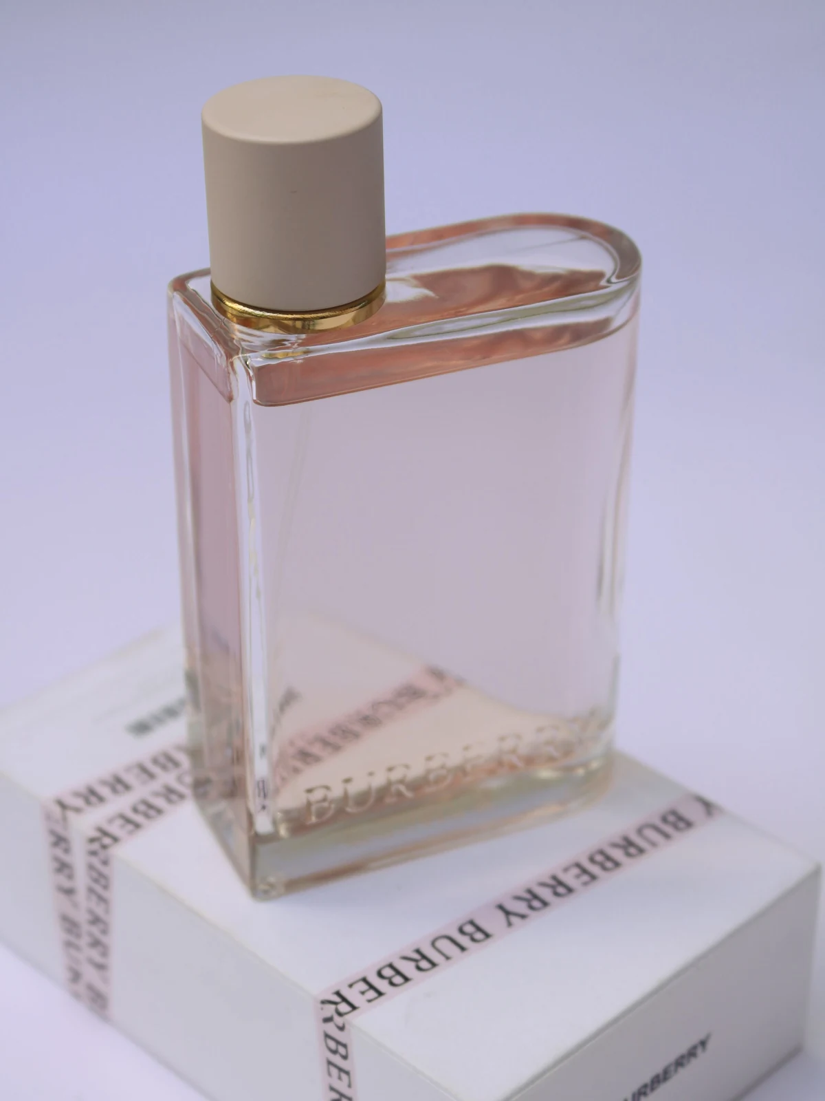 A clear perfume bottle with a cream cap on a branded carton