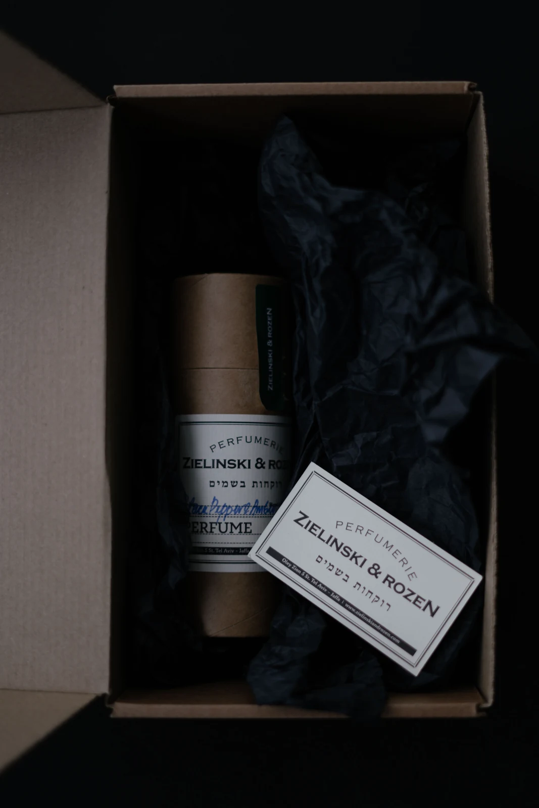 A labelled perfume container and printed card inside an open carton