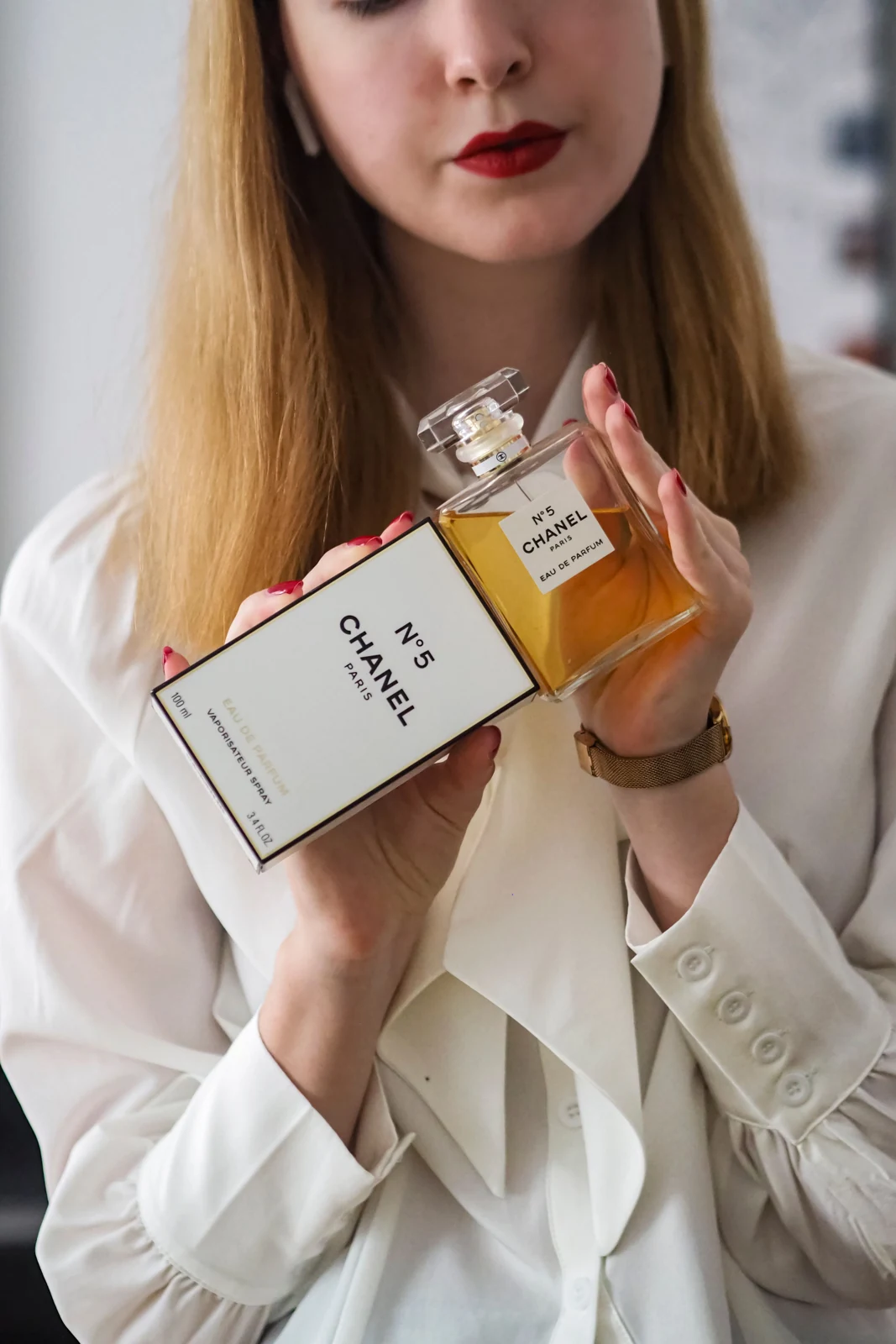 A woman holding a capped perfume bottle beside its printed carton