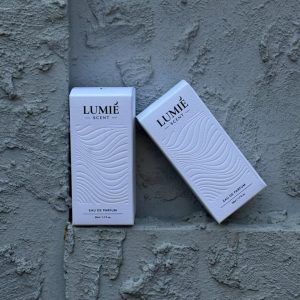 Square product photo of white perfume folding cartons with dark lettering and an embossed wave pattern