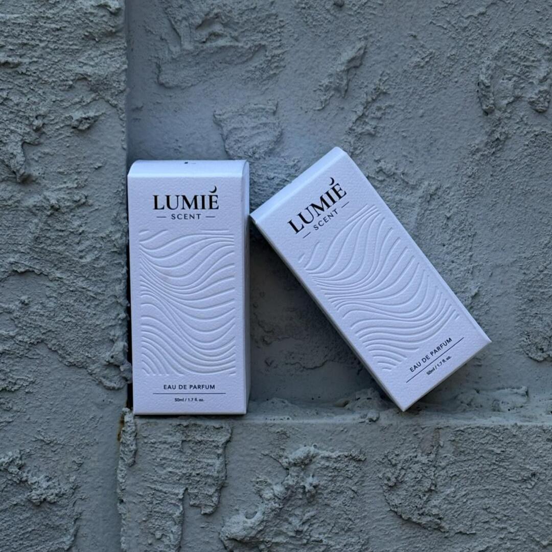 Square product photo of white perfume folding cartons with dark lettering and an embossed wave pattern